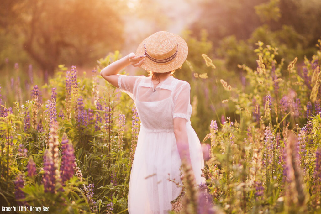 A women standing with her back to the camera in a flower field with her hand on her hat.