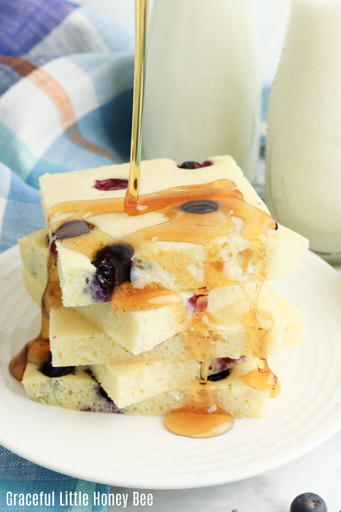 A stack of blueberry pancake squares on a white plate with syrup drizzled on top.