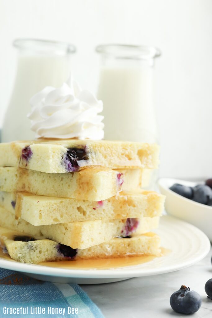 Stack of pancake squares sitting on a plate topped with syrup and whipped cream.