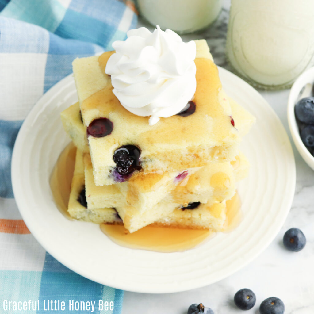 Stack of pancake squares sitting on a plate topped with syrup and whipped cream.