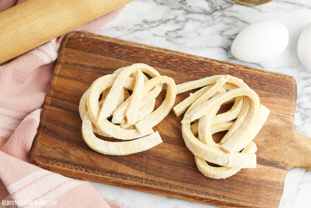 Egg noodles sitting on a wooden cutting board.