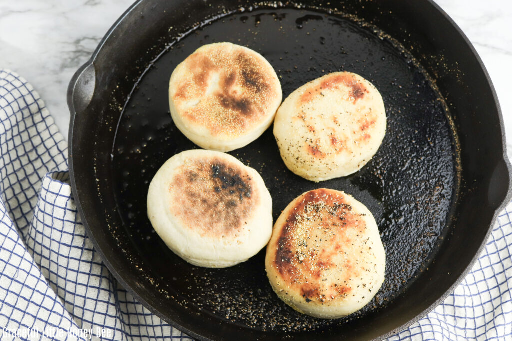 English muffins toasting in a cast iron pan.