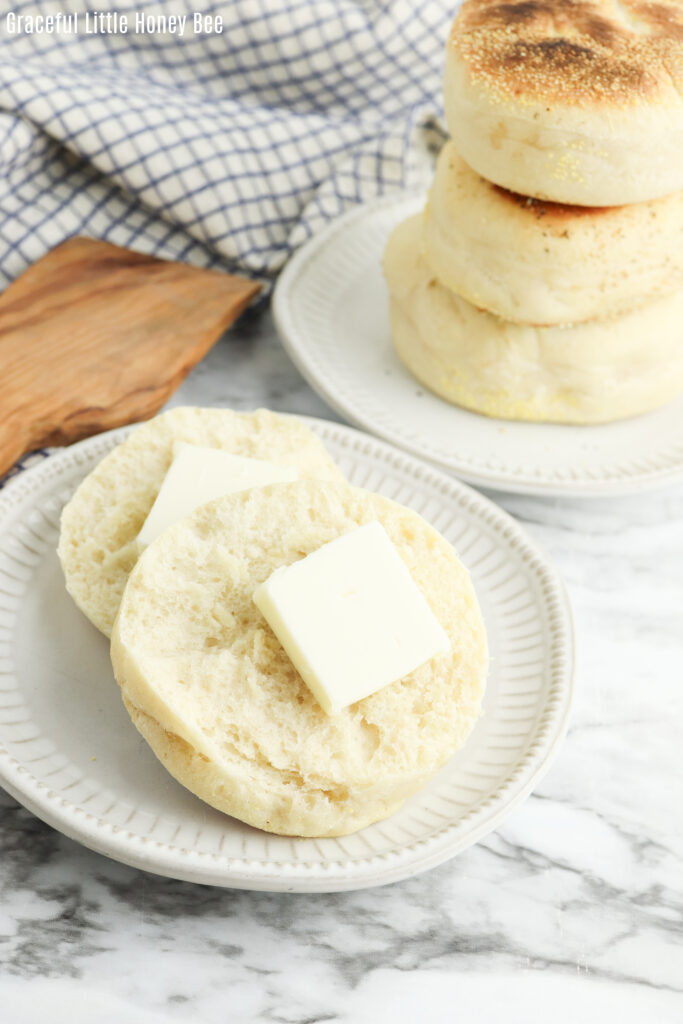 An English muffin cut in half and topped with butter, sitting on a white plate.