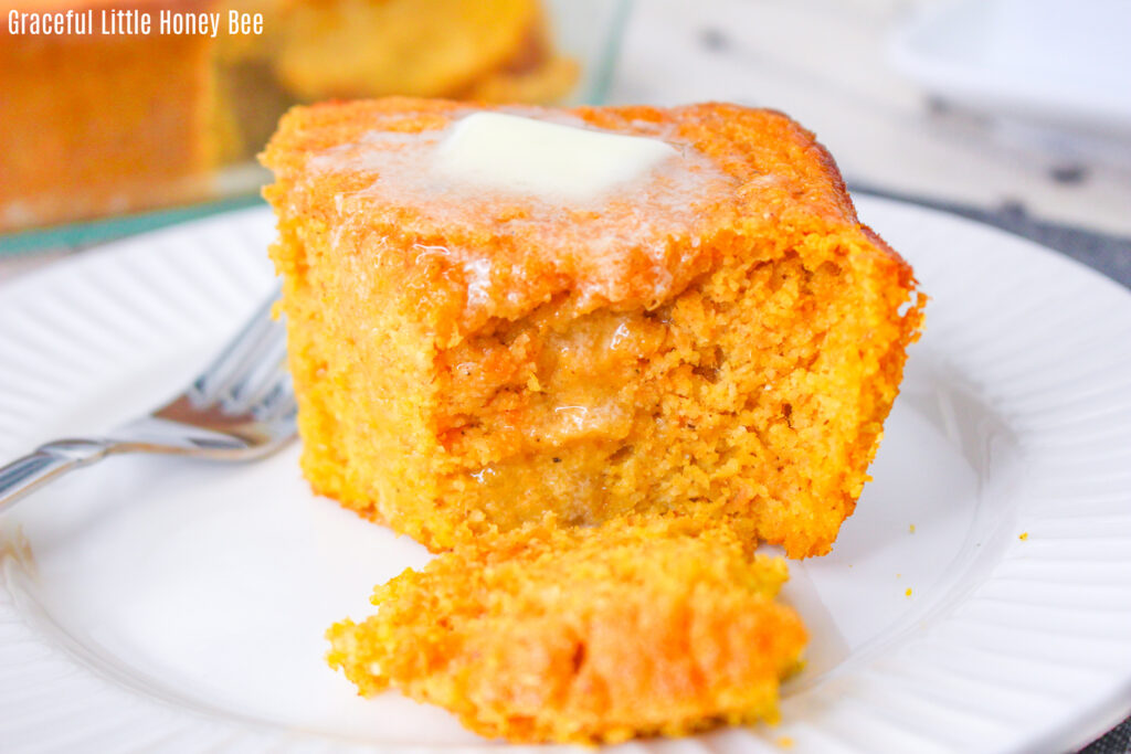 A close up view of a slice of spoonbread with a pat of butter on top.