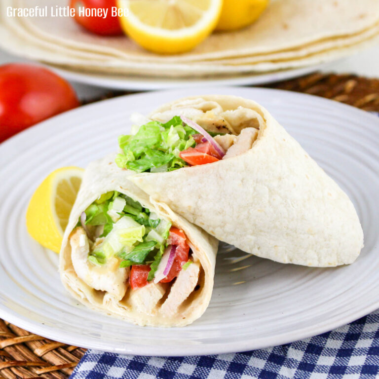 Close up view of a honey mustard chicken wrap cut in half and sitting on a white plate.