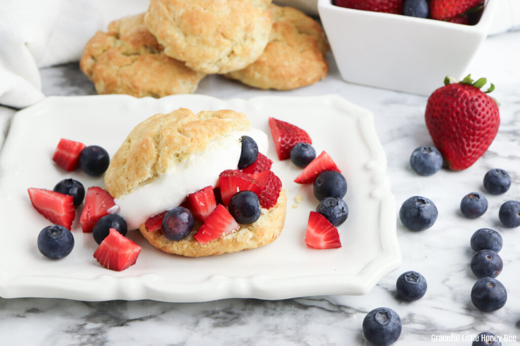 A close up view of a homemade shortcake cut in half and topped with whipped cream and fresh berries.