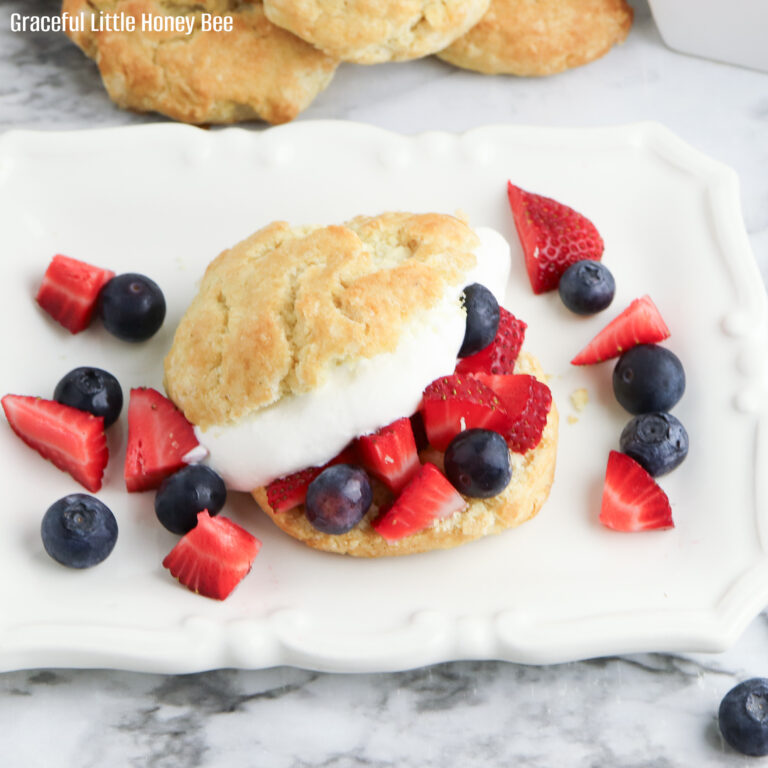 A close up view of a homemade shortcake cut in half and topped with whipped cream and fresh berries.