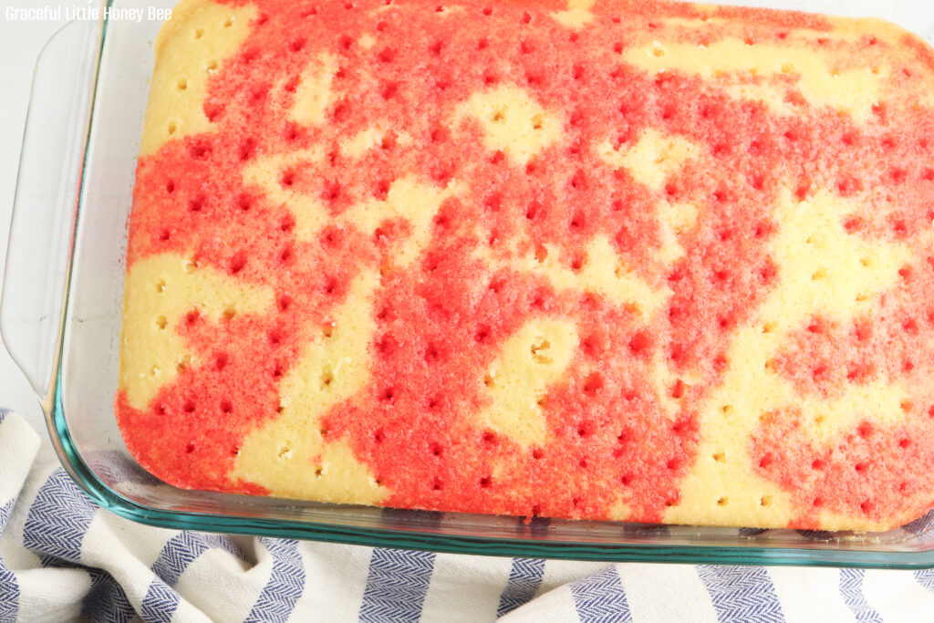 White poke cake with holes poked on top and red jello soaked into it.