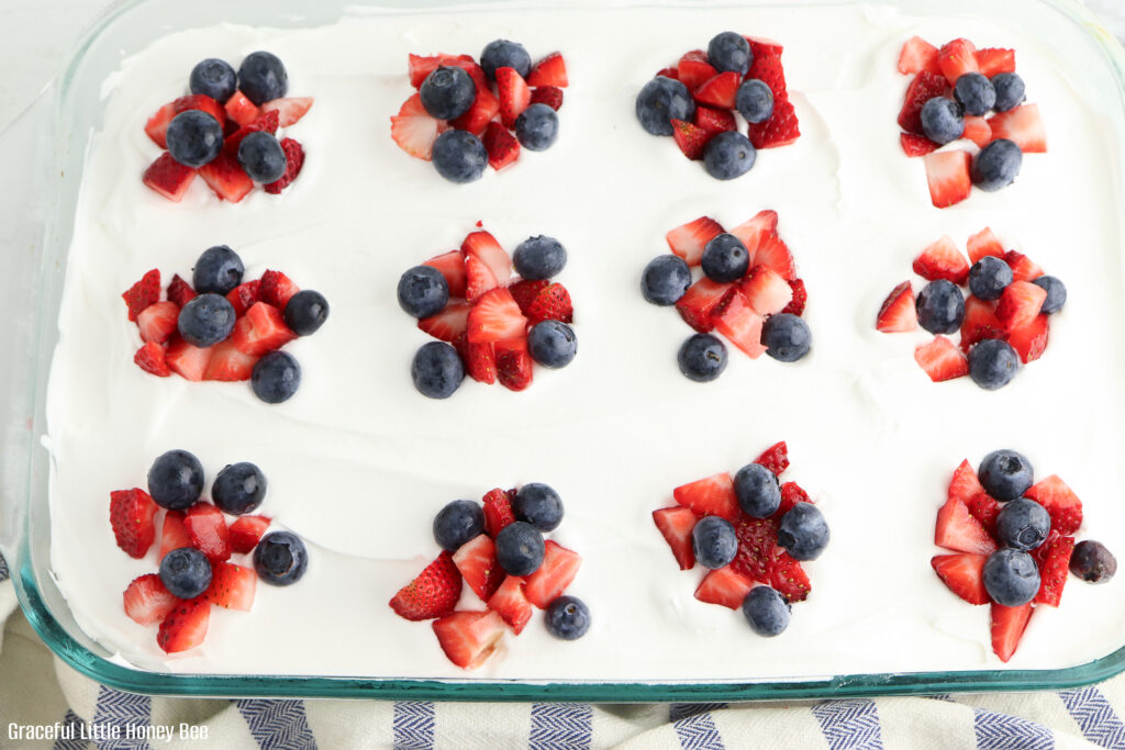 Top view of poke cake topped with whipped topping and small stacks of fresh fruit.