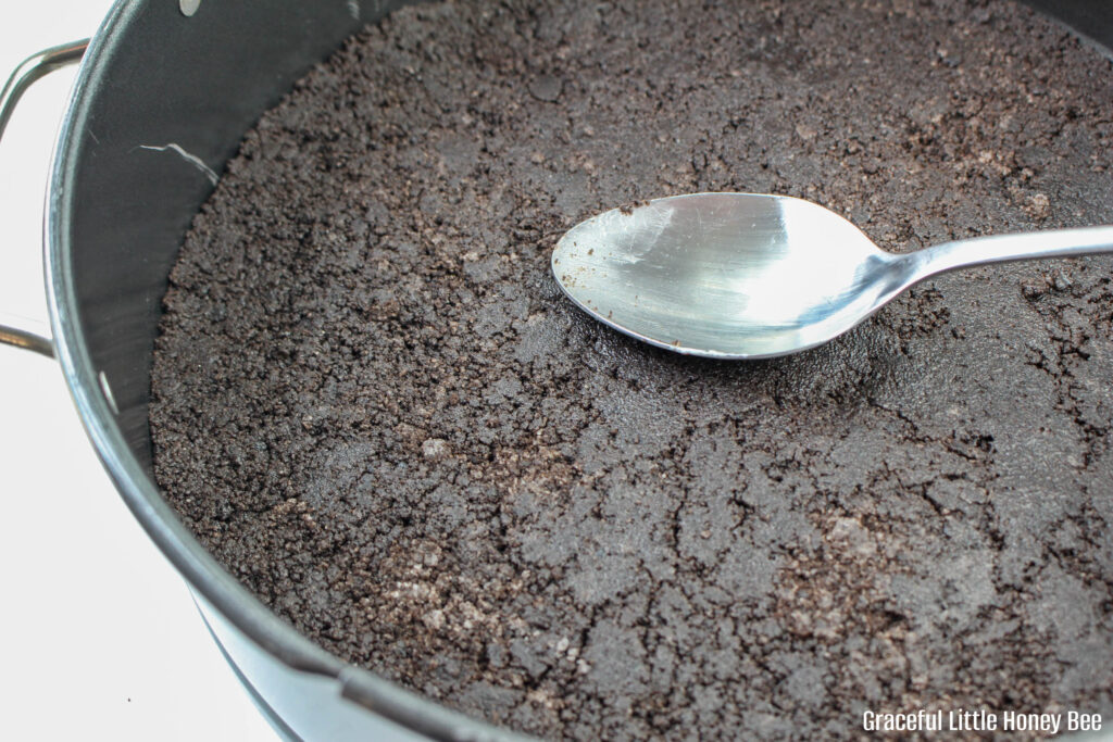 Oreo crust being pressed into a pan.