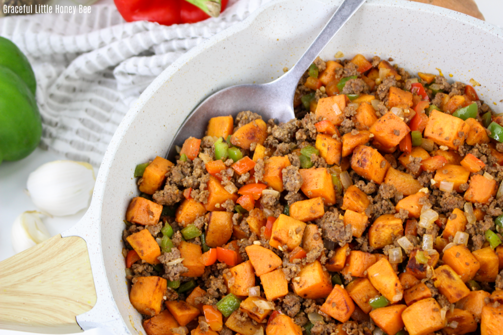 Close up view of beef & sweet potato hash in a white skillet.