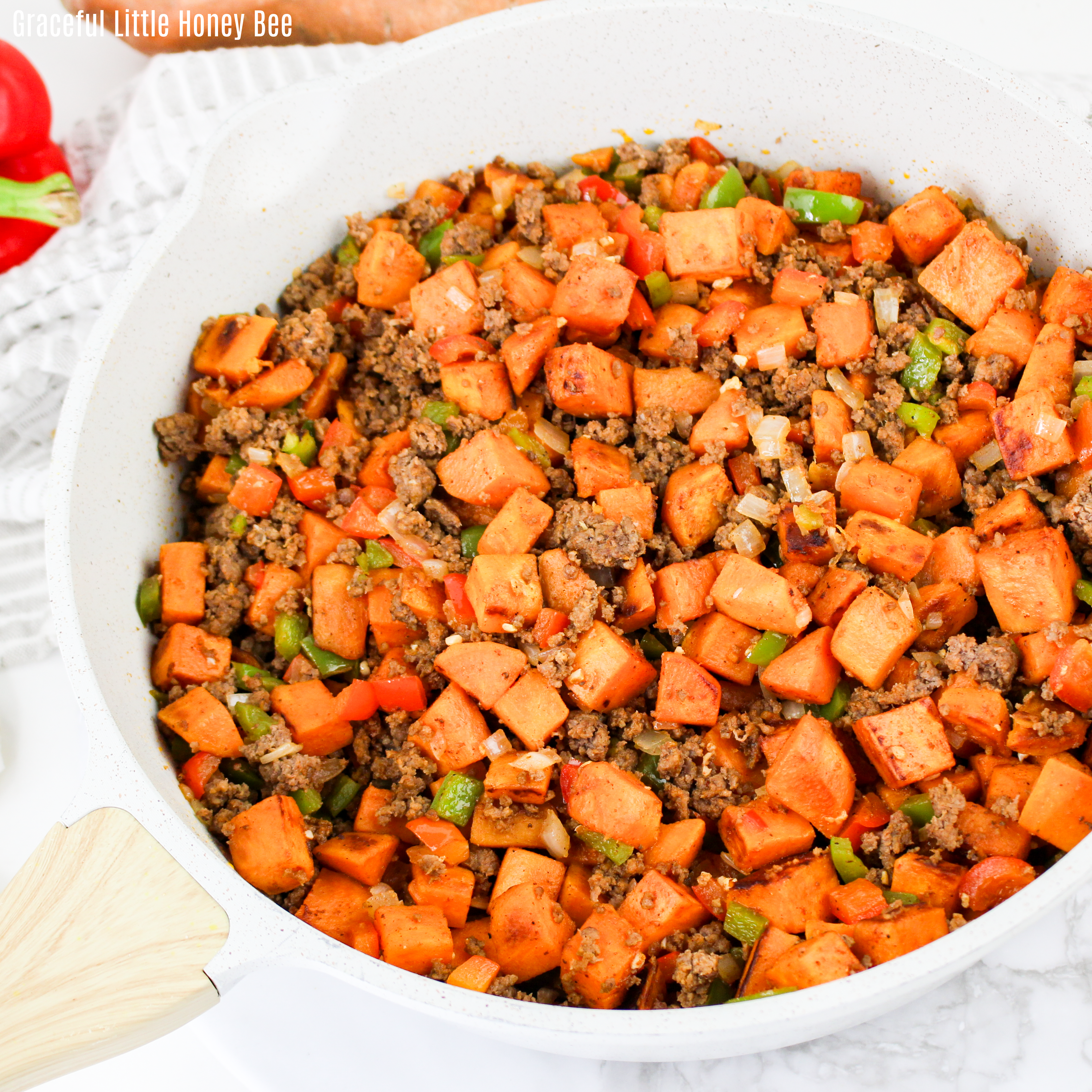 Close up view of beef & sweet potato hash in a white skillet.