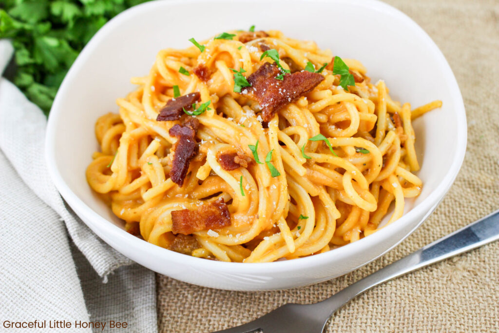 A close up view of pumpkin carbanara garnished with bacon and herbs in a round, white bowl.