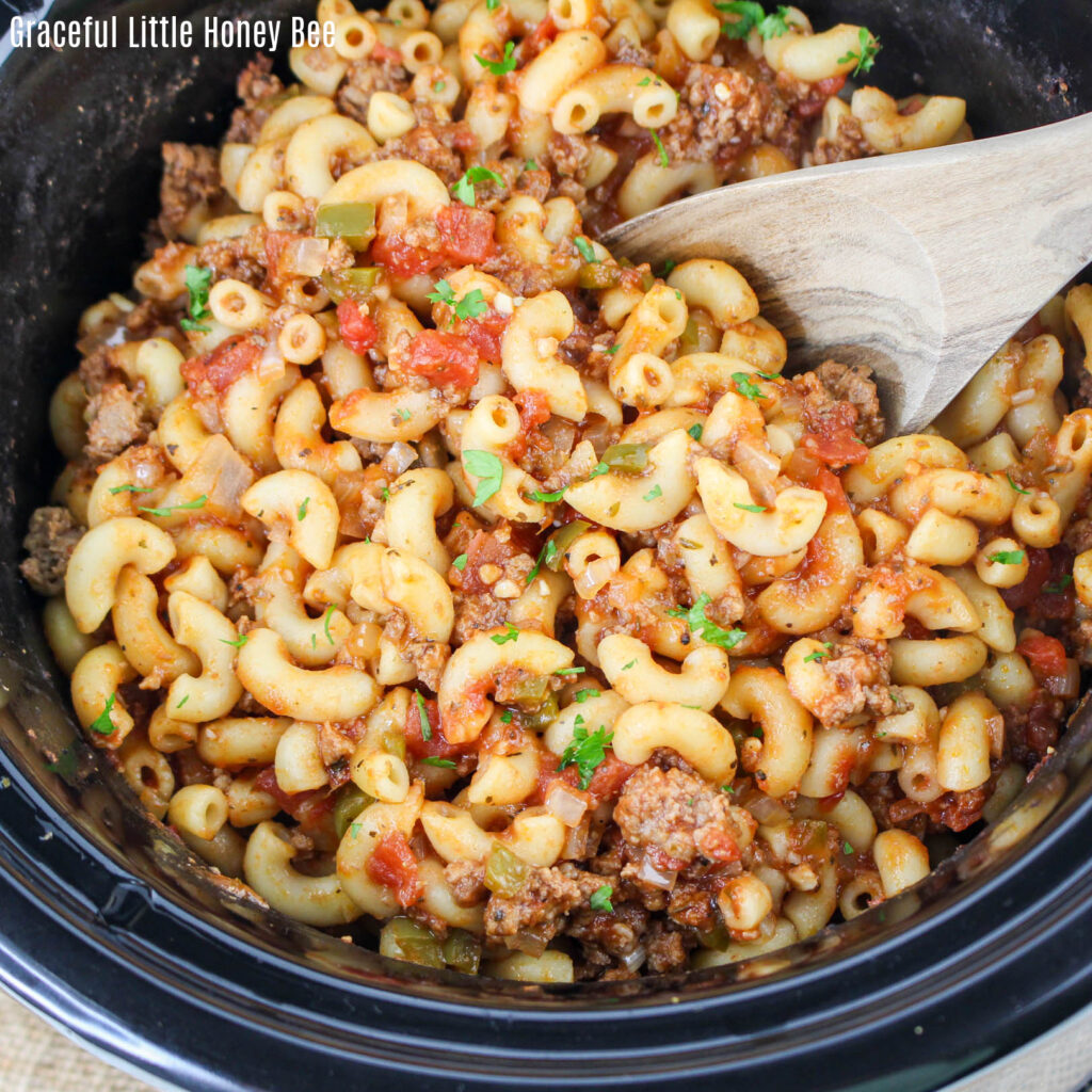 Close up view of goulash in slow cooker with a wooden spoon.