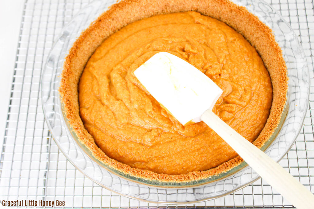 Sweet potato pie filling being spread out onto graham cracker crust with a white spatula.