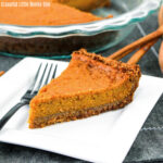 A slice of sweet potato pie on a square white plate with a fork sitting next to it.