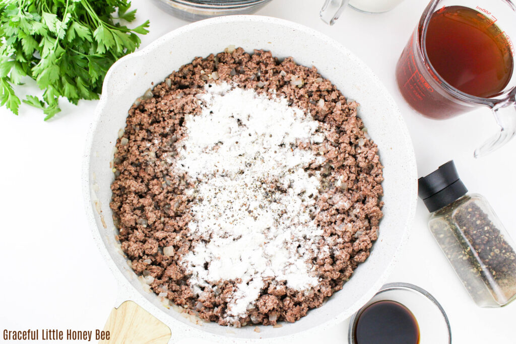 Cooked ground beef in skillet with flour sprinkled over the top.