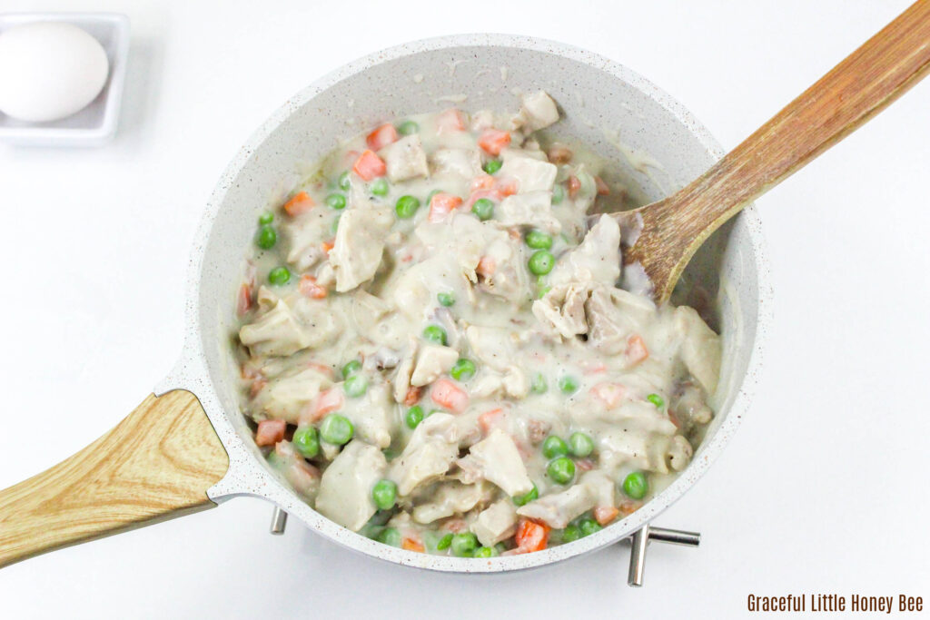 Pot Pie filling in a saucepan with a wooden spoon.