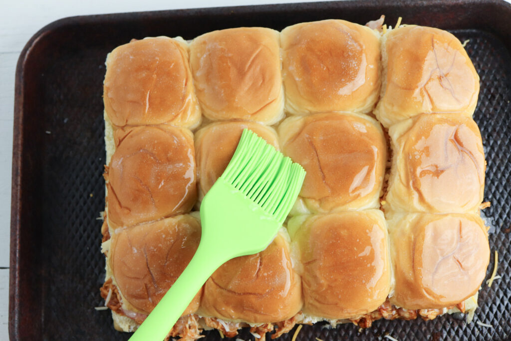 Top of slider buns with butter being spread over the top.