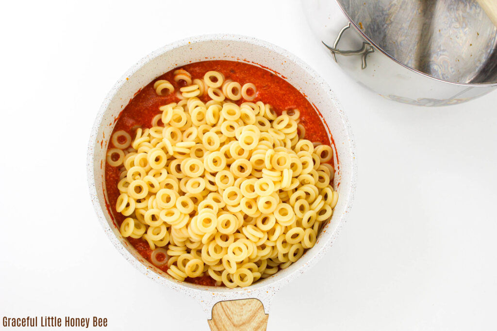 Tomato soup with round circle pasta sitting on top in a saucepan.