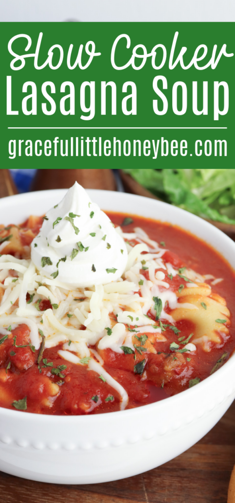 Lasagna Soup in a white bowl topped with shredded mozzarella and sour cream.