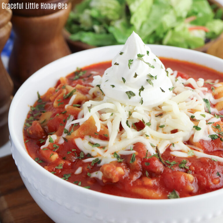 Lasagna Soup in a white bowl topped with shredded mozzarella and sour cream.