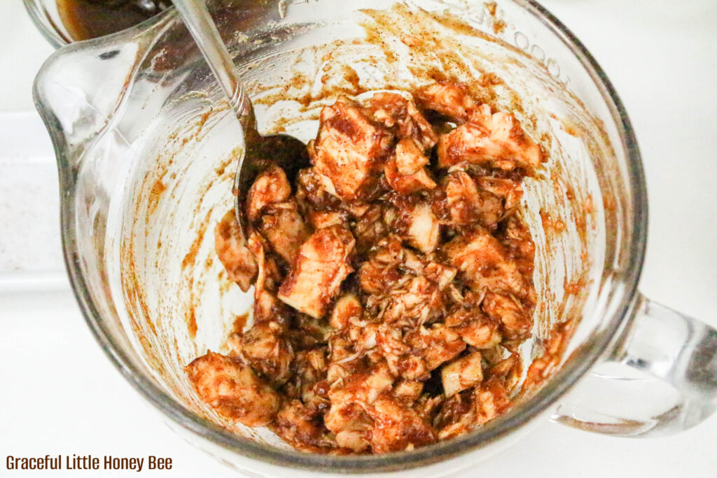 BBQ Sauce and chunks of chicken mixed together in a mixing bowl.