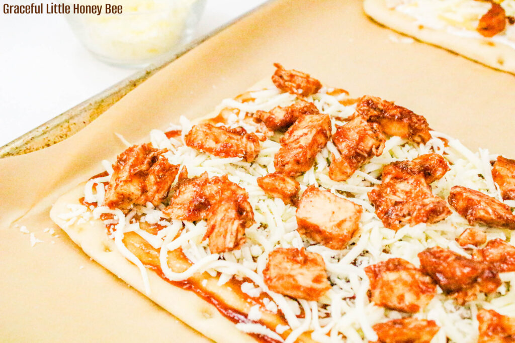 Top view of flatbread topped with BBQ sauce, cheese and chicken.