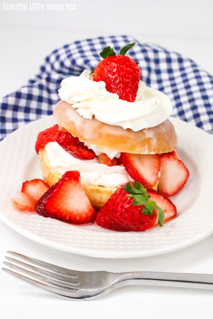 A glazed donut cut in half then filled and topped with whipped cream and strawberries.