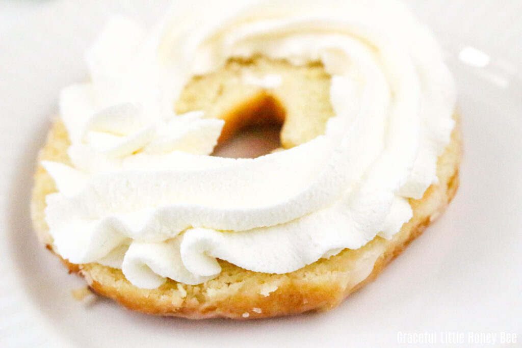 The bottom of a sliced glazed donut with whipped cream piped around the top.