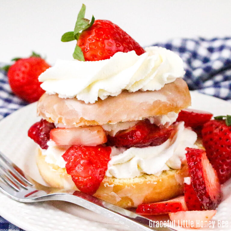 A glazed donut cut in half then filled and topped with whipped cream and strawberries.