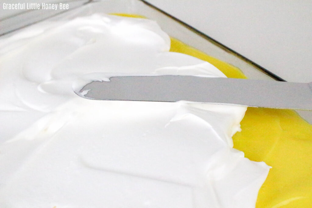 Whipped topping being spread over the top of a lemon cake.