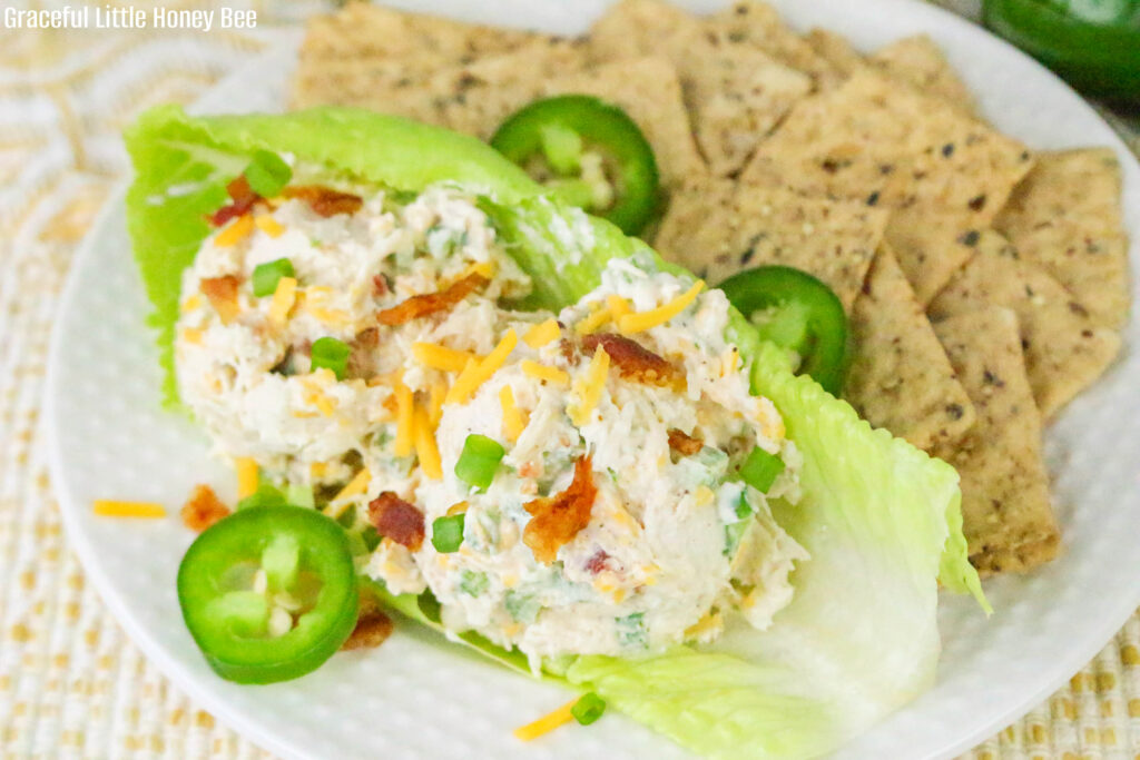 Two large scoops of Jalapeno Popper Chicken Salad on a crisp lettuce leaf served with chips on a white plate.