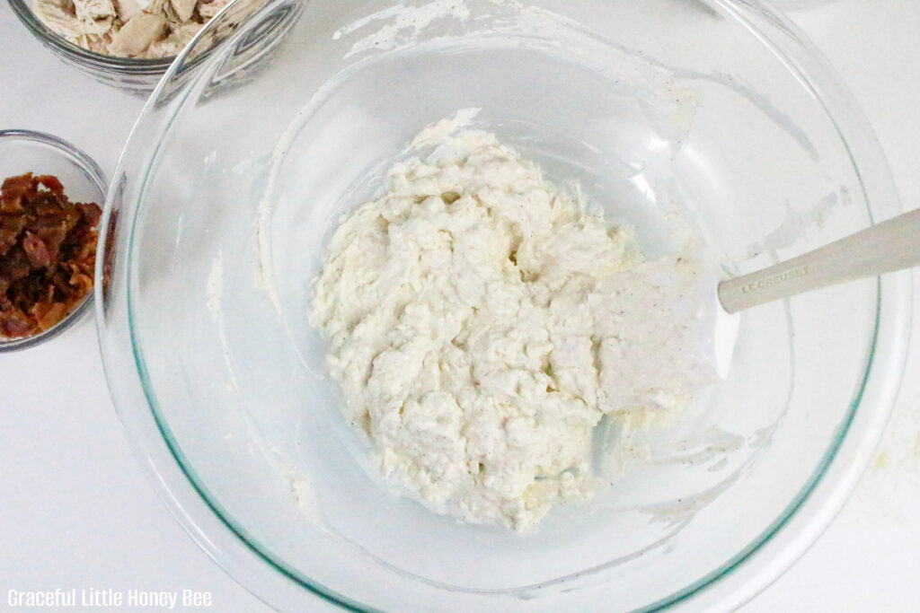 Cream cheese, mayo and spices in a clear glass mixing bowl.