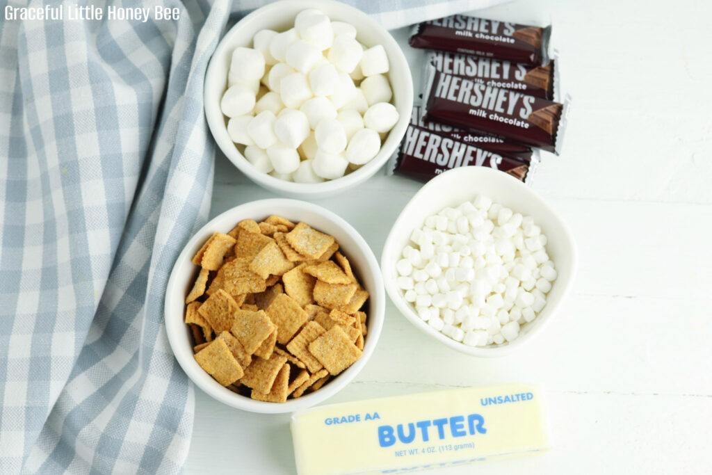 A stick of butter, mini marshmallows, mini chocolate bars and graham cereal sitting on the counter.