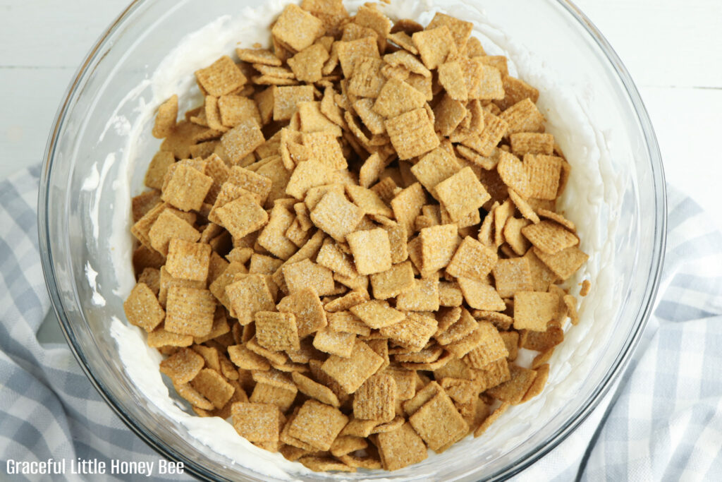 Graham cracker cereal with marshmallow and butter mixture in mixing bowl.