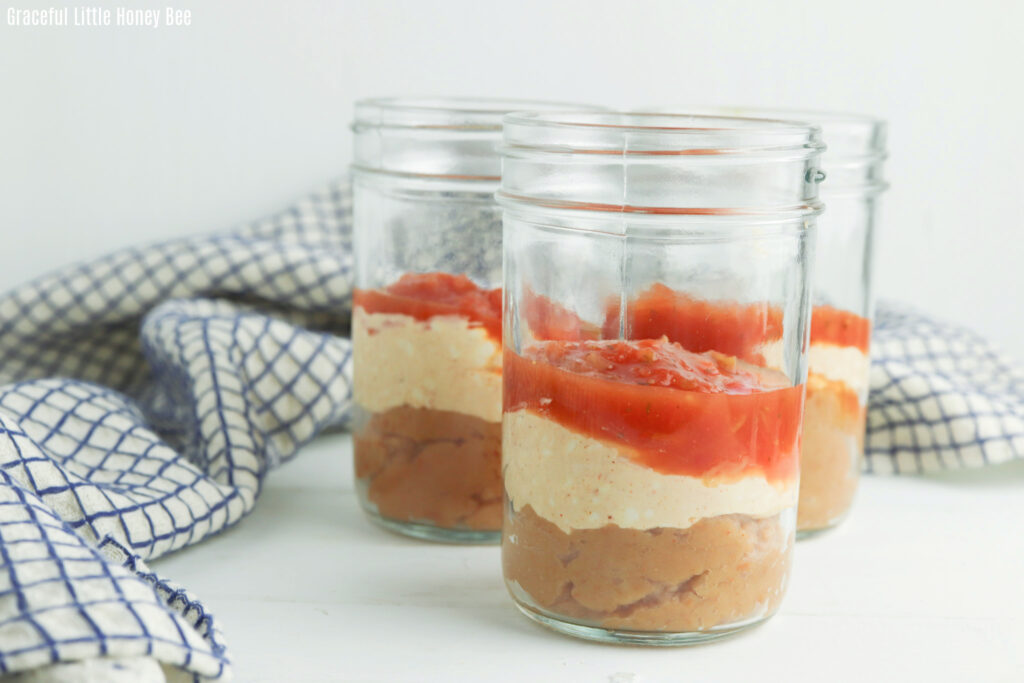 Side view of beans, sour cream and salsa layered in a jar.