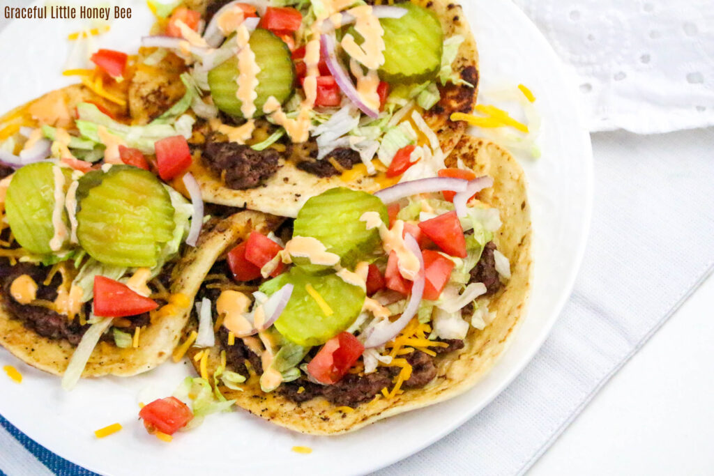 Aerial view of three smash burger tacos on a white plate.