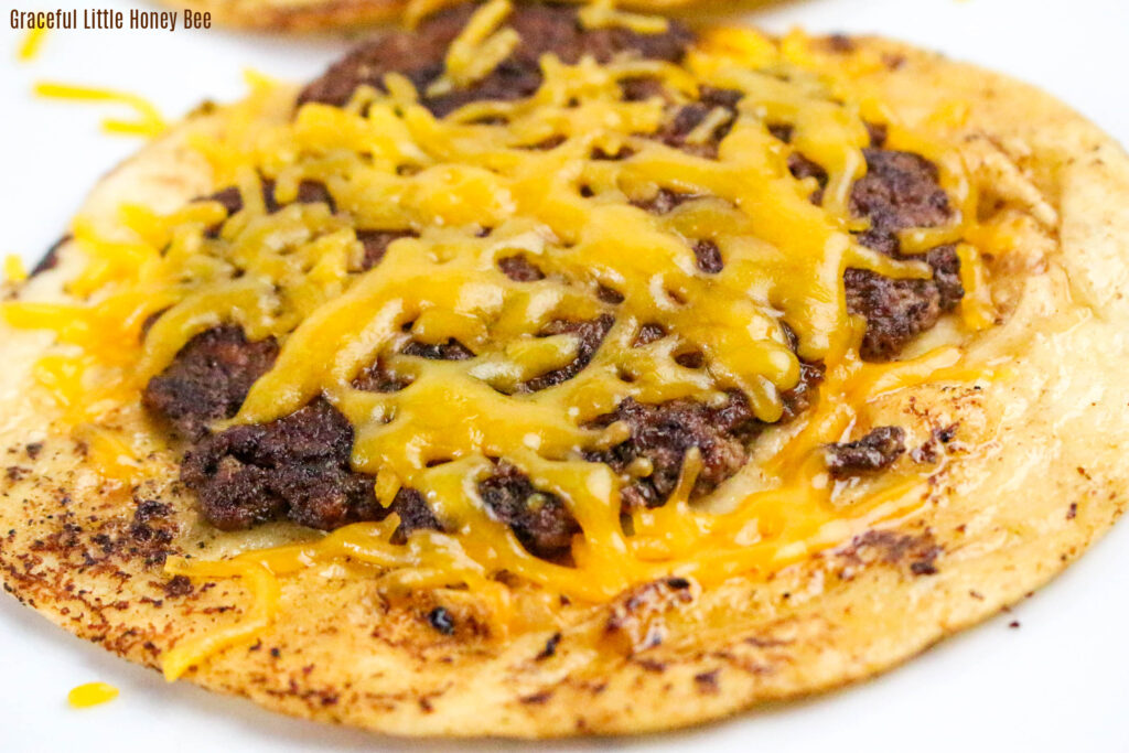 A crispy tortilla topped with golden brown ground beef and melted cheddar cheese.