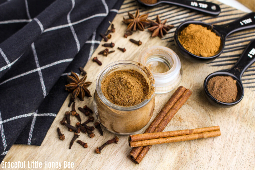 Top view of pumpkin pie spice in a glass jar with dish towel and whole spices in the background.