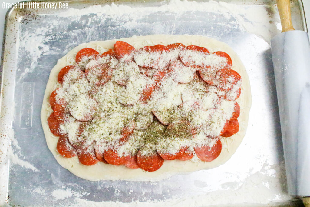 Pizza dough topped with cheese, pepperoni and spices before being rolled up.