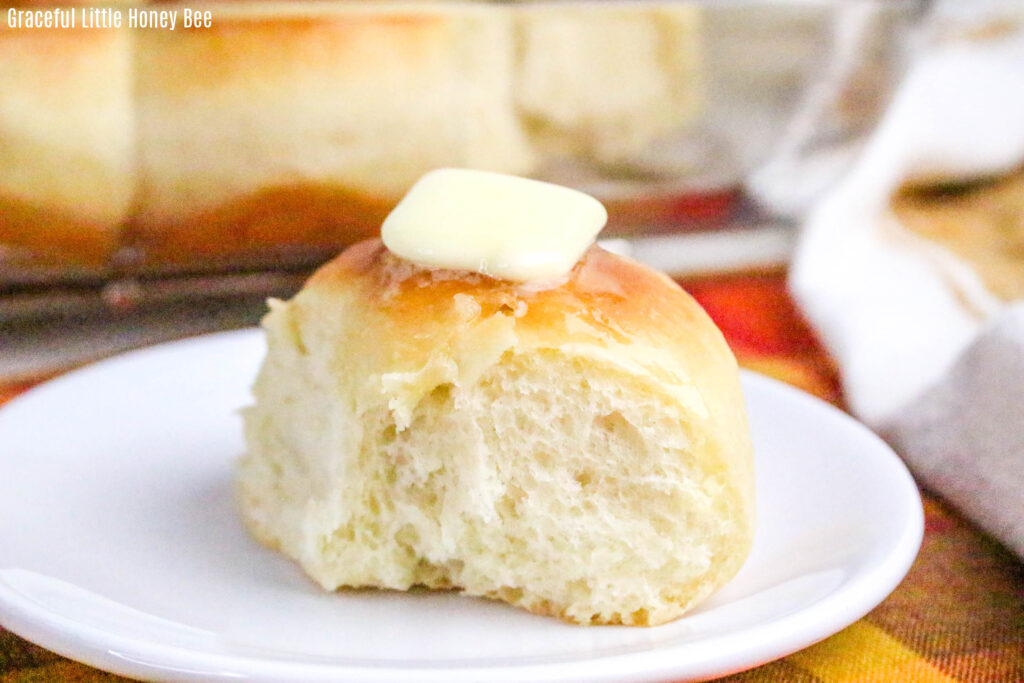 Side view of a dinner roll topped with butter on a white plate.