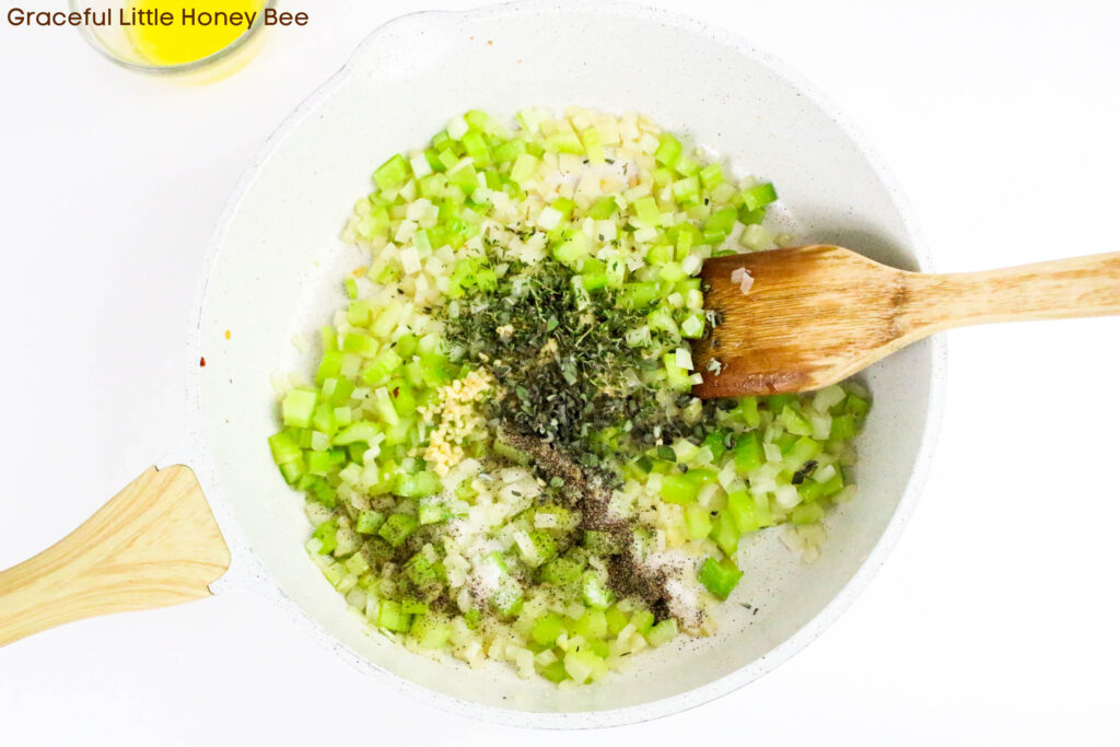 Celery, onions and herbs being sauteed in a pan.