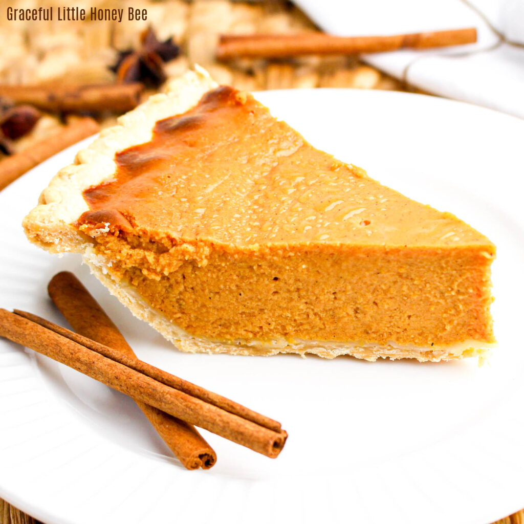 Slice of pumpkin pie with cinnamon sticks on a white plate.