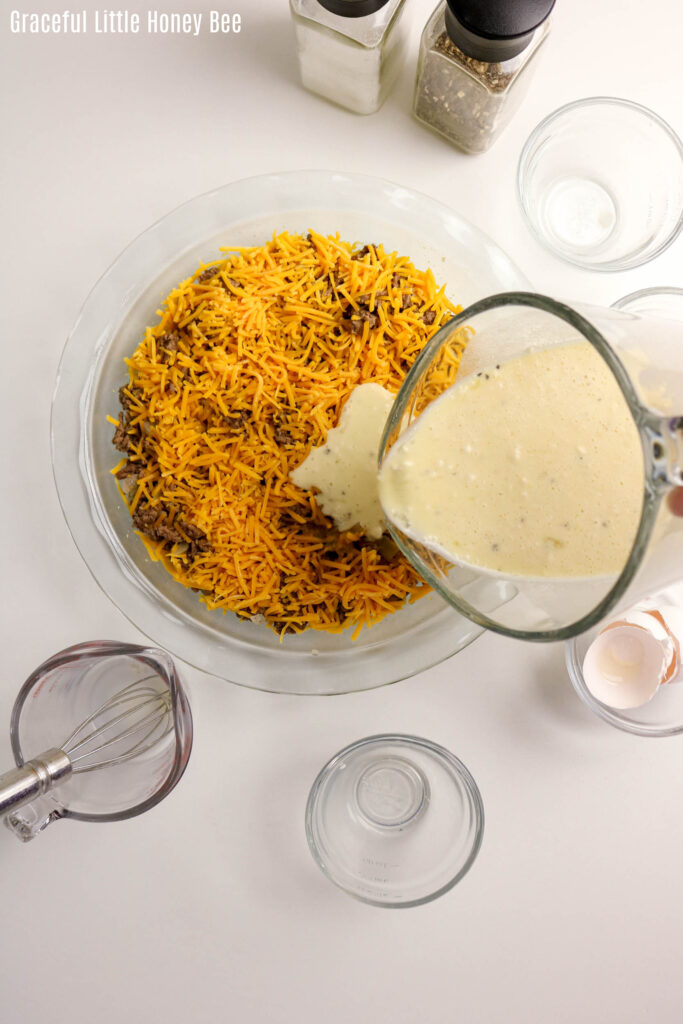 Aerial view of beef and cheese mixture in glass pie dish with batter being poured over the top.