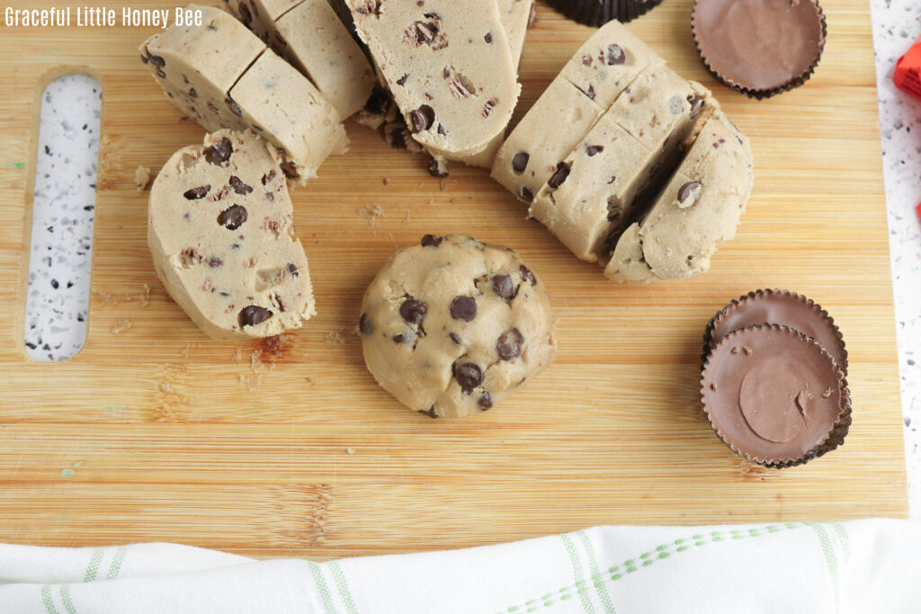 Cookie dough sliced on a cutting board with a Reese's stuffed cookie dough.