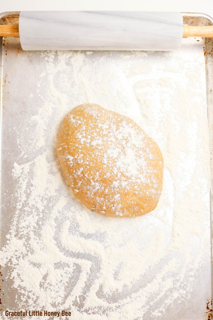 Cinnamon roll dough in a ball on a floured surface next to a rolling pin.