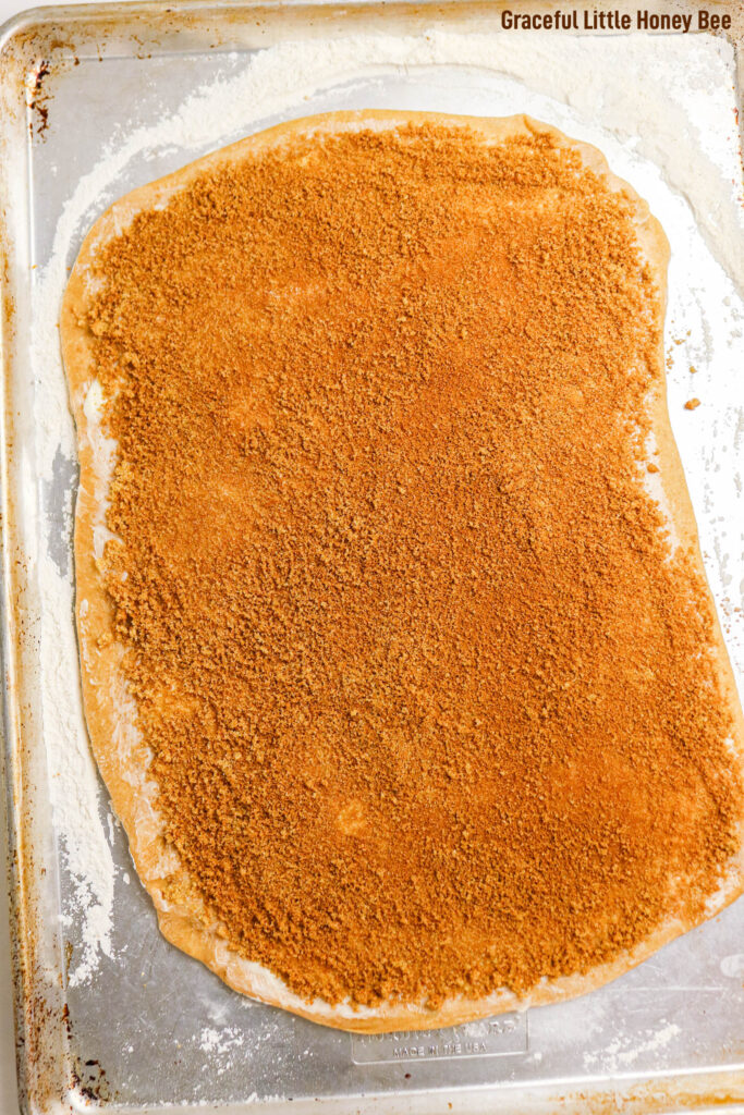 Cinnamon roll dough sprinkled with cinnamon and sugar rolled out into a rectangle.