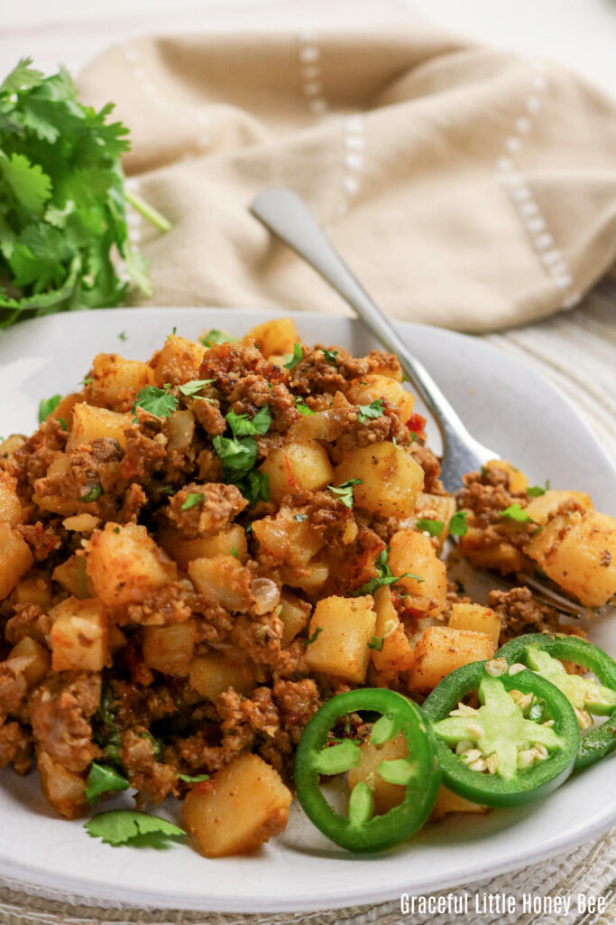 Serving of ground beef & potatoes on a white plate with a spoon sitting next to it.