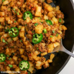 Ground beef & potatoes in a skillet topped with fresh slices of jalapenos.